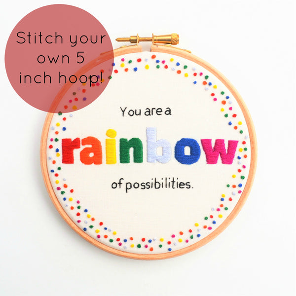 A wooden embroidery hoop with the quote You are a rainbow of possibilities  with the word rainbow in bold rainbow coloured letters with a coordinating french knot border. 